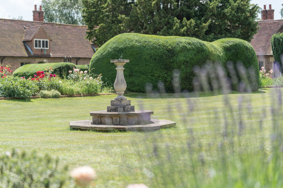 Fountain set in mown lawn with large clipped yew hedge in background